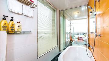 A modern bathroom with a bathtub, a glass shower enclosure, and a window with blinds.