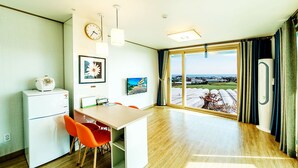A modern kitchen with a dining area, a clock, and a large window with a view of the countryside.