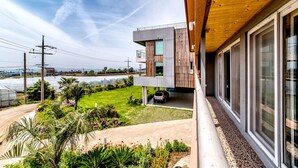 A modern two-story house with a balcony overlooking a garden and a view of the sea.