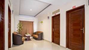 Un hall de hotel con dos sofás, una mesita, una planta en maceta y dos puertas de madera.