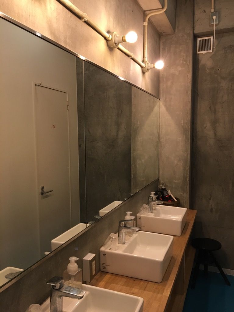 A modern bathroom with a large mirror, three sinks, and a black stool.