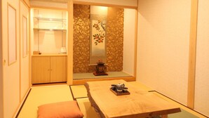 A traditional Japanese room with tatami flooring, a low wooden table, cushions, and a sliding door leading to a kitchen area. - Ichinomatsu Japanese Modern Hotel (Takayama)