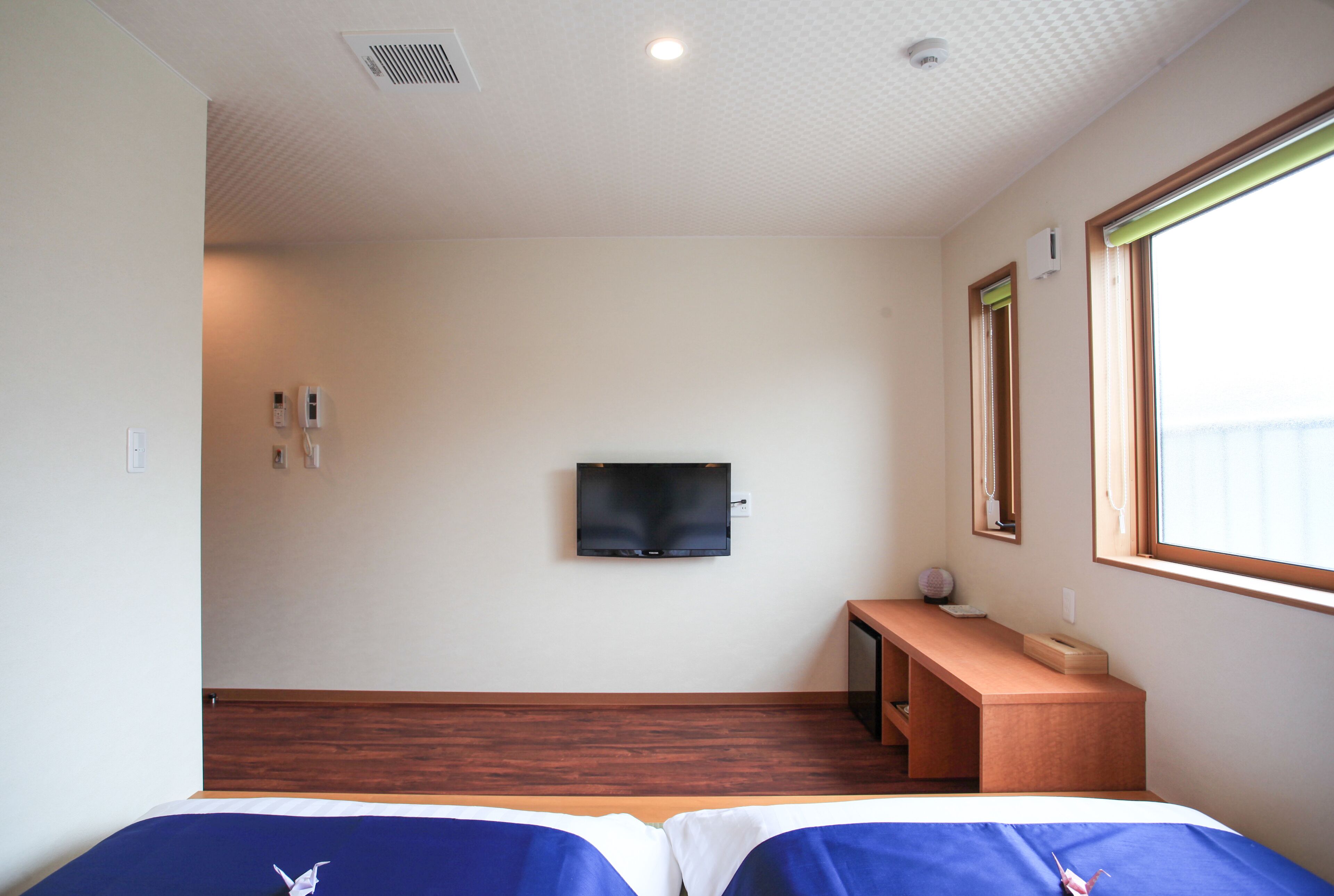 A hotel room with a bed, a TV mounted on the wall, a desk, and a window.