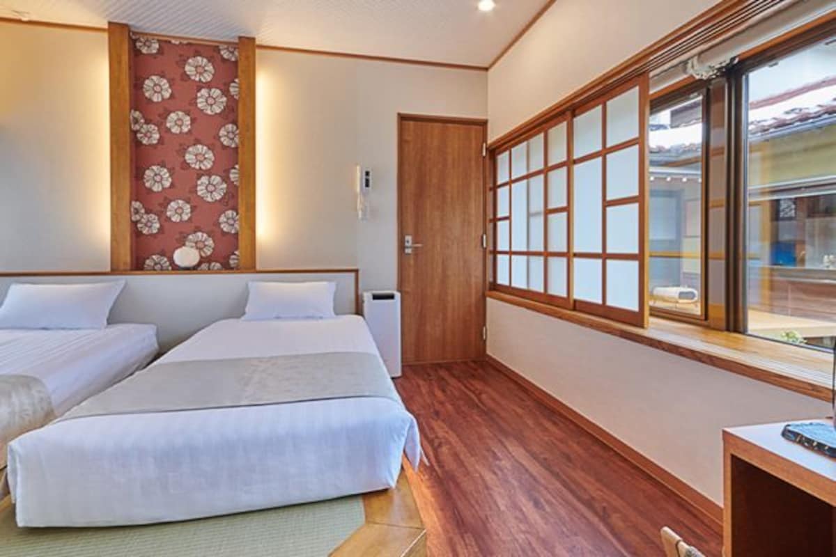 Une chambre d’hôtel avec deux lits, un plancher en bois, une grande fenêtre donnant sur un beau paysage et un lambris mural de style traditionnel.