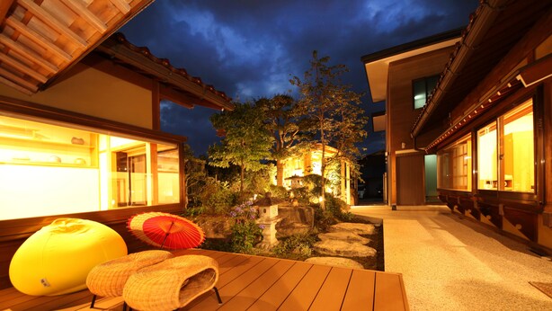 A wooden deck with seating and a small water feature, surrounded by buildings with warm lighting. - Ichinomatsu Japanese Modern Hotel (Takayama)