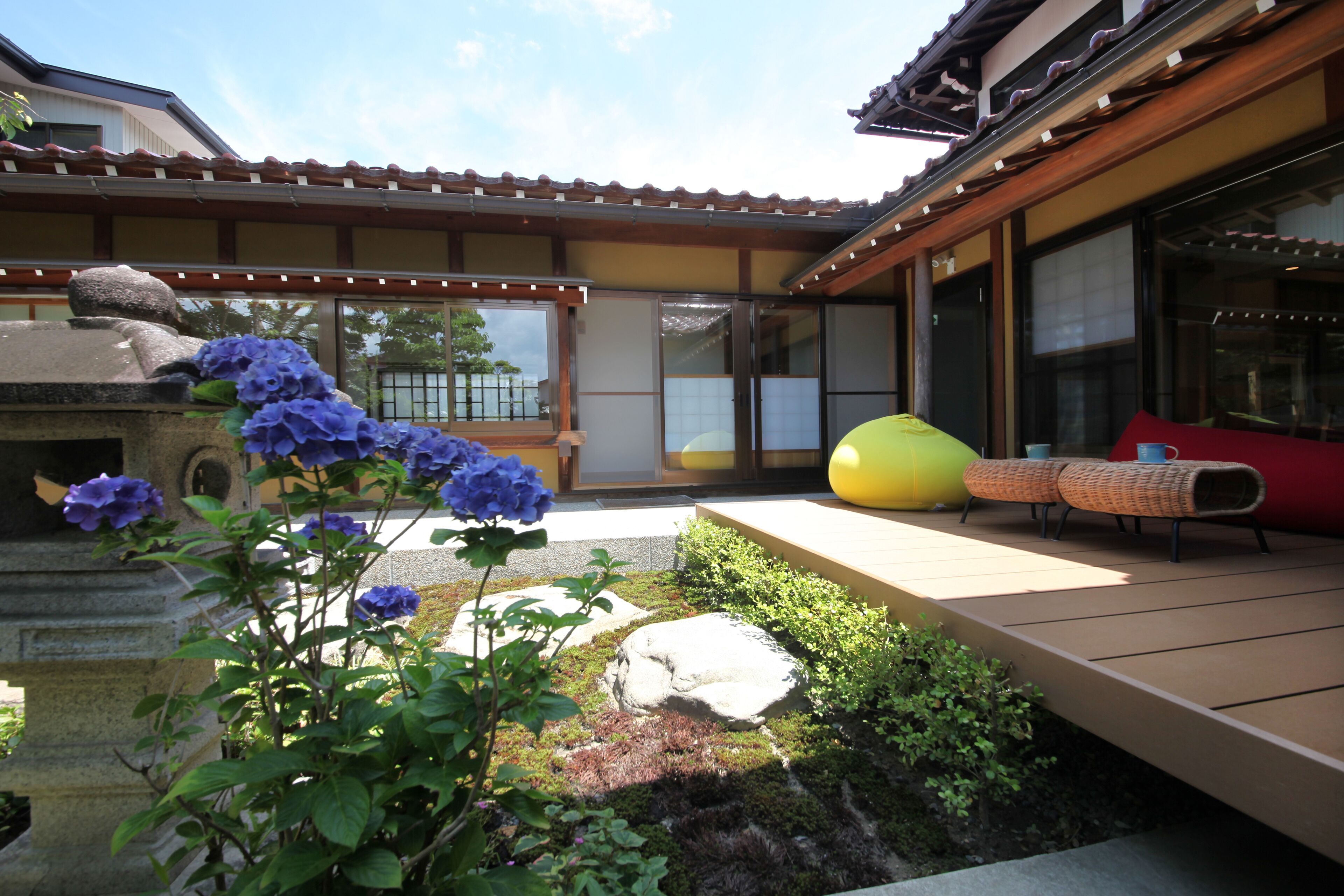 Un edificio tradicional japonés con suelo de tatami, un farolillo de piedra y un jardín con rocas, plantas y un arbusto de hortensia azul.
