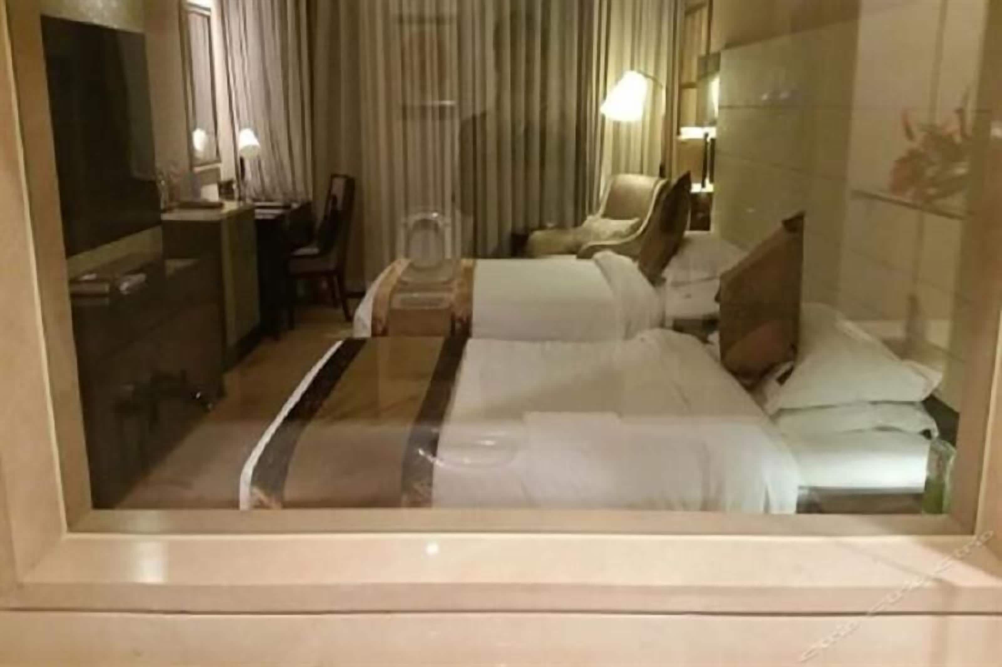 Una habitación de hotel con una cama, un escritorio, una silla, un espejo y una ventana con cortinas.