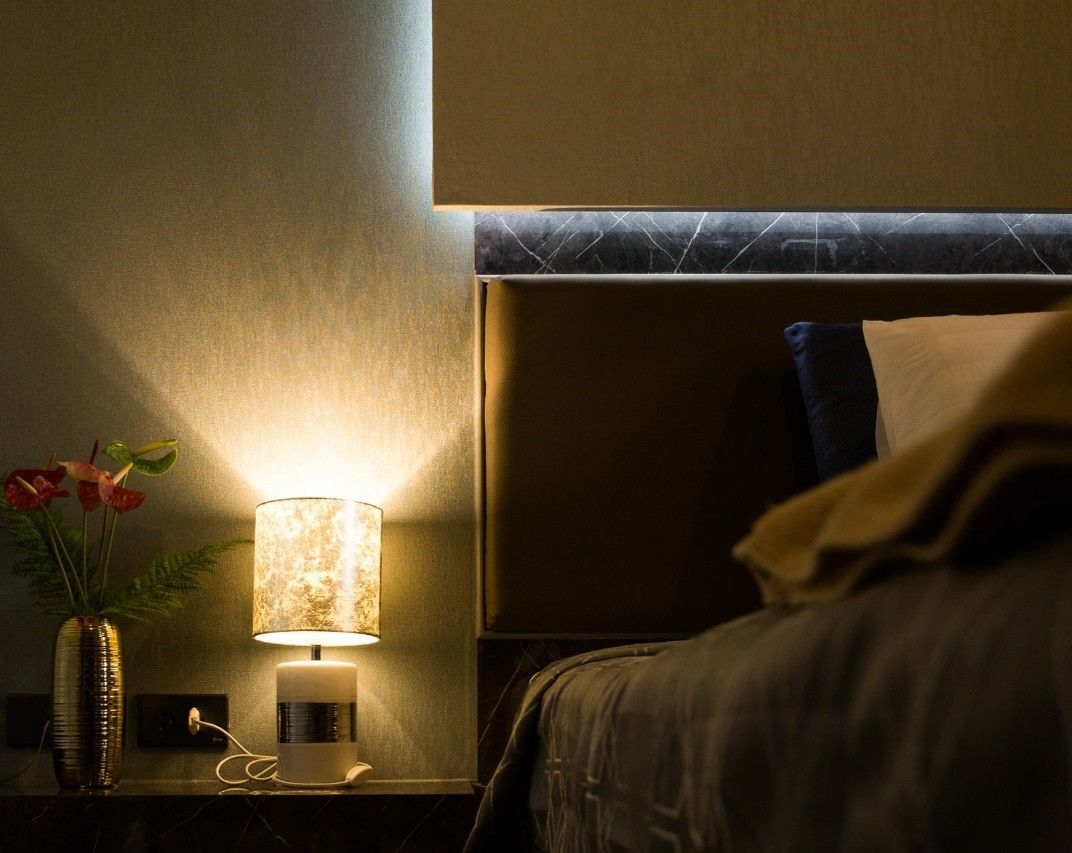 A hotel room with a bedside lamp, a vase with flowers, and a bed with a headboard.
