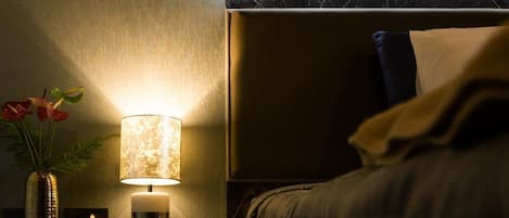 A hotel room with a bedside lamp, a vase with flowers, and a bed with a headboard.