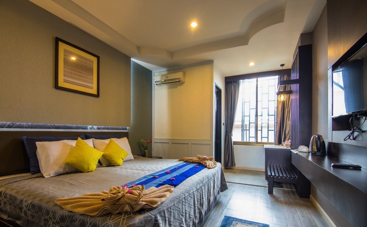 A hotel room with a bed, a desk, a TV, and a window with curtains.
