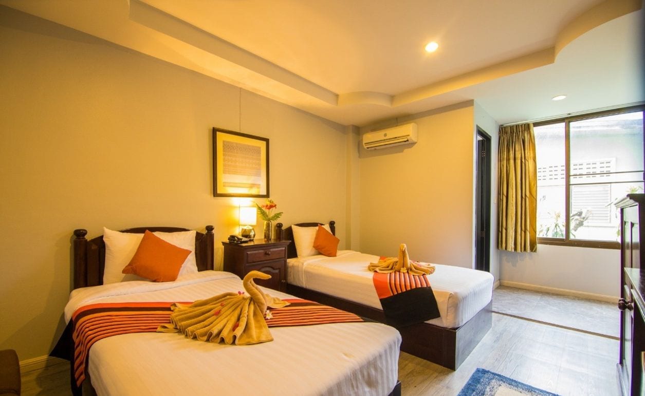 Quarto de hotel com duas camas, um certificado emoldurado na parede, ar condicionado e uma janela com cortinas.