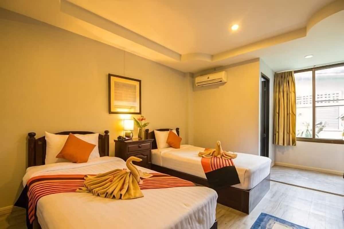 A hotel room with two beds, a nightstand with a lamp, a framed picture on the wall, and a window with curtains.