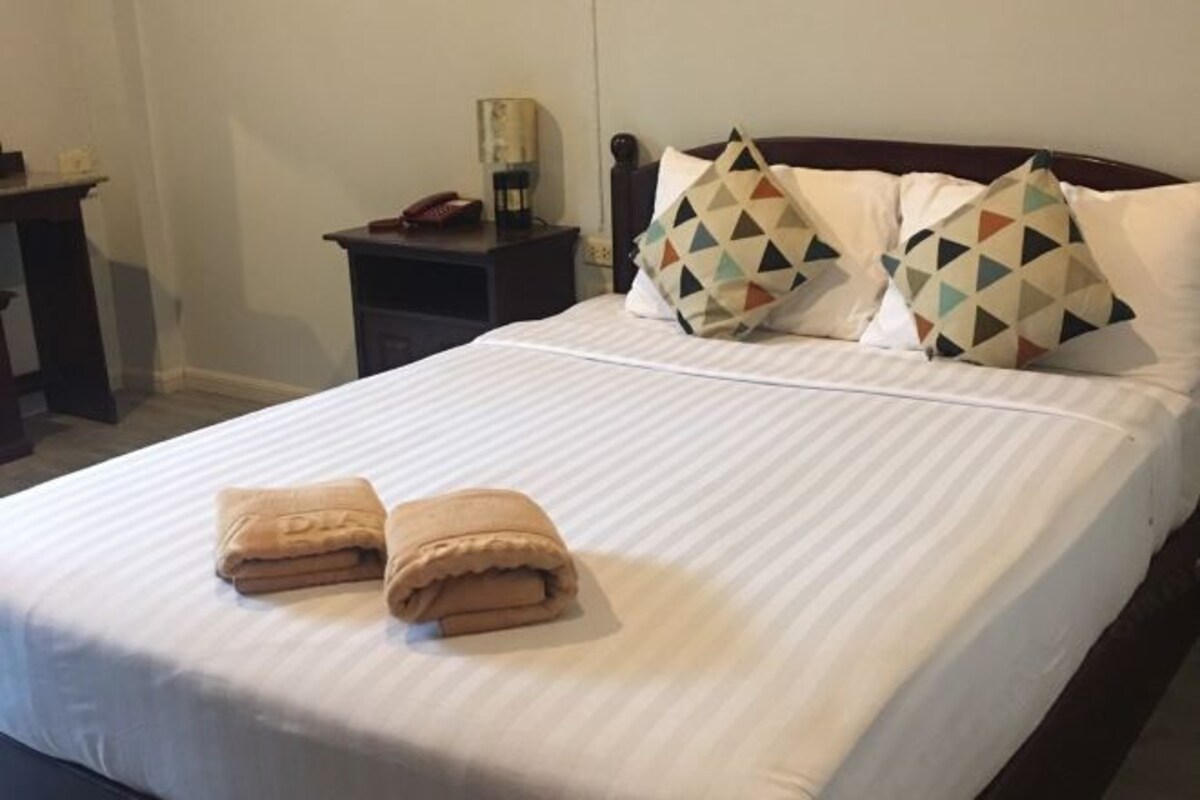 Una cama bien tendida con dos toallas dobladas, una mesita de noche con una lámpara y un aparador con un teléfono.