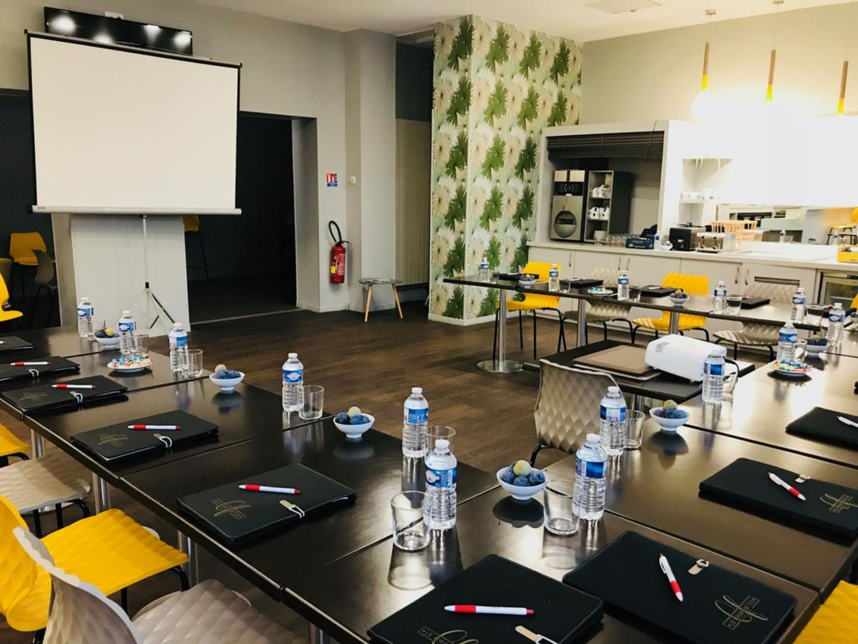 A conference room with a long table, chairs, water bottles, and a projector screen.