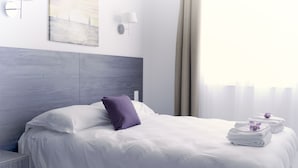 A modern hotel room with a large bed, a headboard, a wall-mounted light, and a window with curtains. - Hôtel Le Chapon Fin (Moissac)