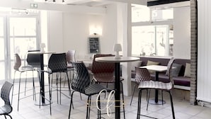 A modern cafe interior with round tables and black chairs, a chalkboard menu, and a view of the street through large windows. - Hôtel Le Chapon Fin (Moissac)