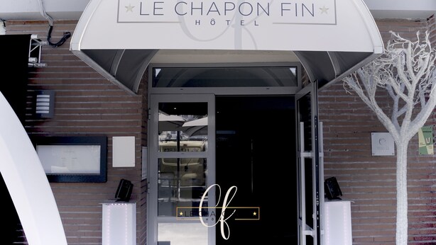 The entrance of Le Chapon Fin Hotel with a modern design, featuring a glass door and a sign above. - Hôtel Le Chapon Fin (Moissac)