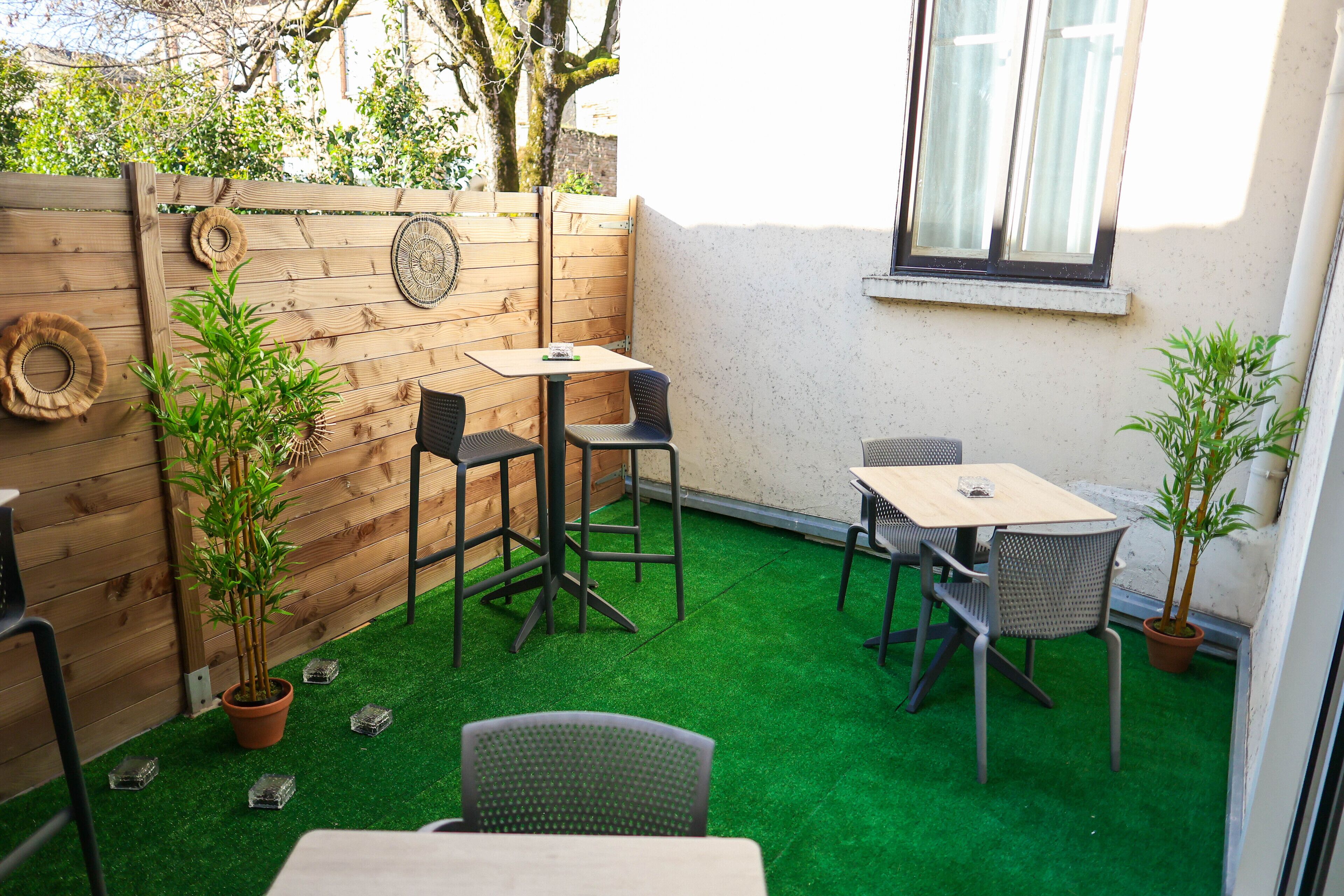 A small patio area with a wooden fence, a table, two chairs, and potted plants.