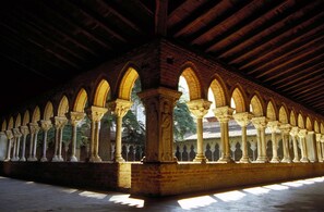An interior with a series of arches supported by columns, a vaulted ceiling, and a brick wall. - Hôtel Le Chapon Fin (Moissac)