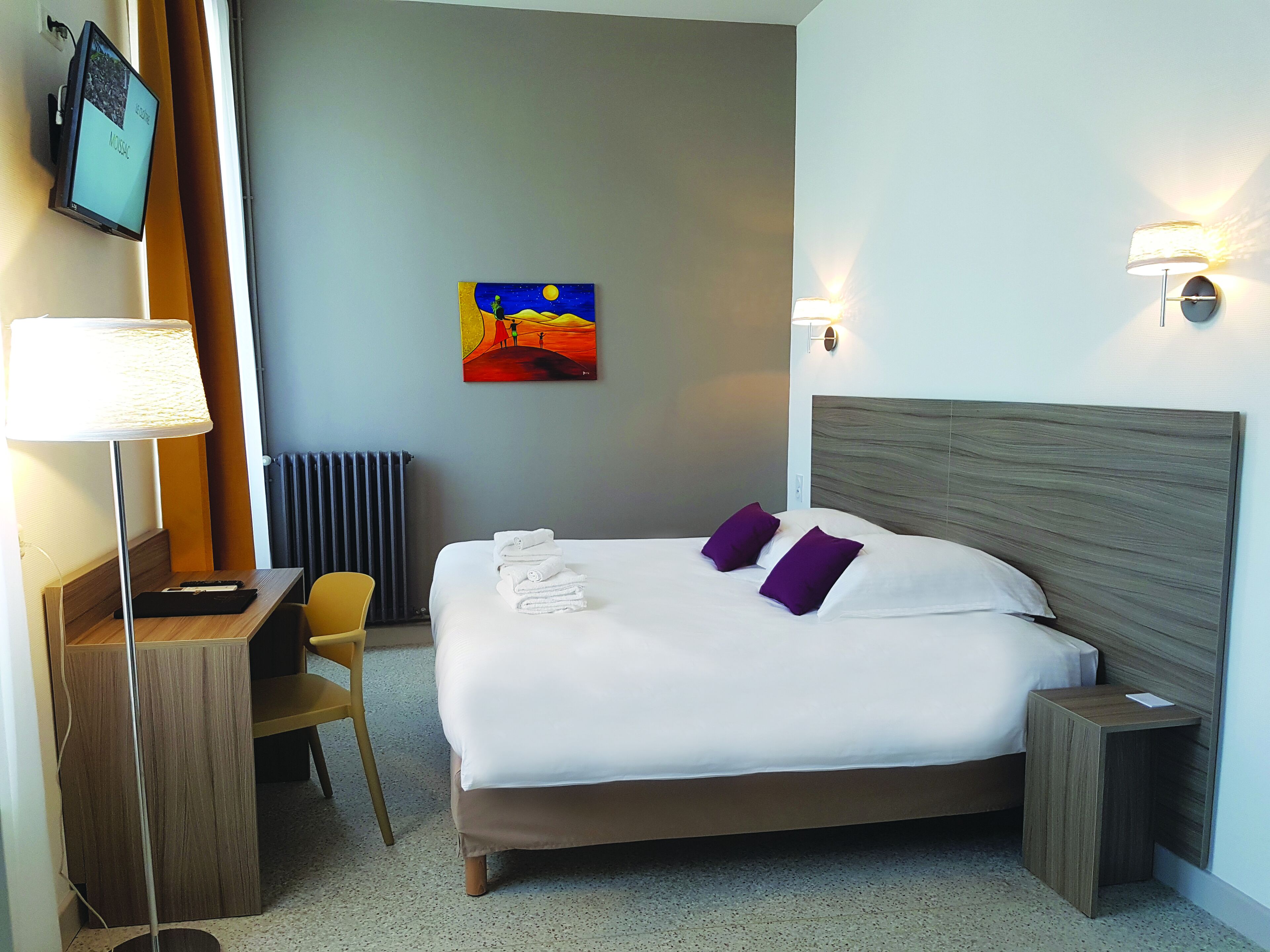 Ein Hotelzimmer mit Bett, Schreibtisch, Stuhl, Fernseher und Bildern an der Wand.