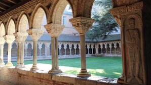 A cloister with a series of arches and columns, a brick building in the background, and a grassy courtyard. - Hôtel Le Chapon Fin (Moissac)
