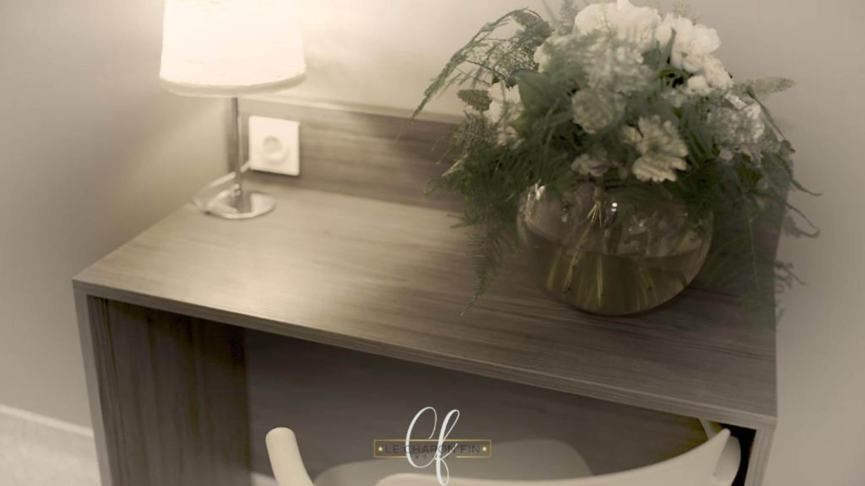 Un baño con tocador de madera, una silla blanca y una planta en maceta con flores blancas.