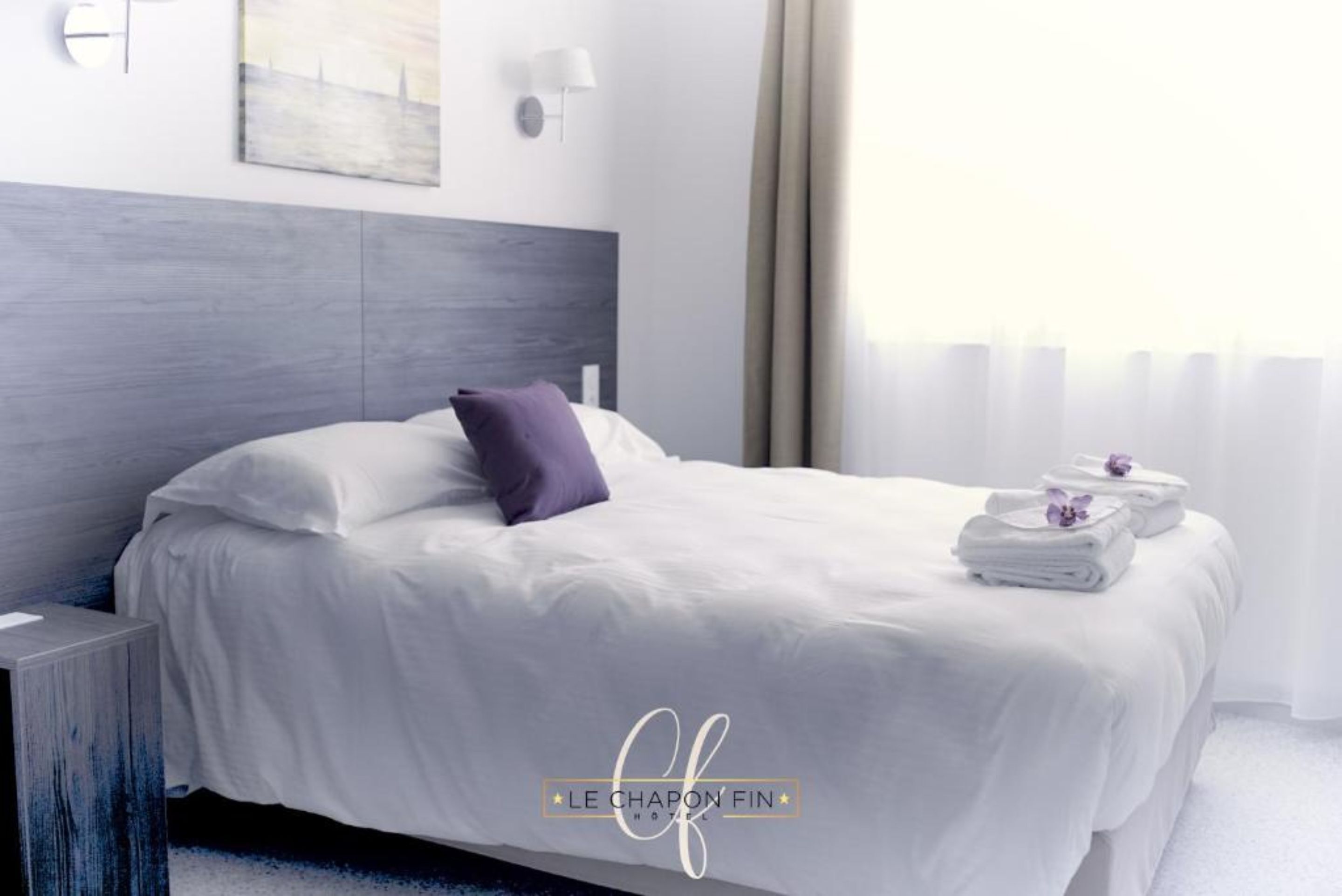 A modern hotel room with a neatly made bed, a side table, and a view of the city through the window.