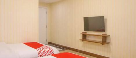 A hotel room with two beds, a television on a shelf, and a door.