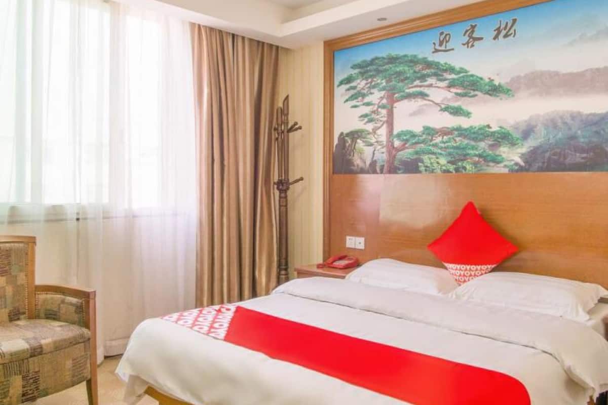A hotel room with a bed, a chair, a painting, and a window with curtains.