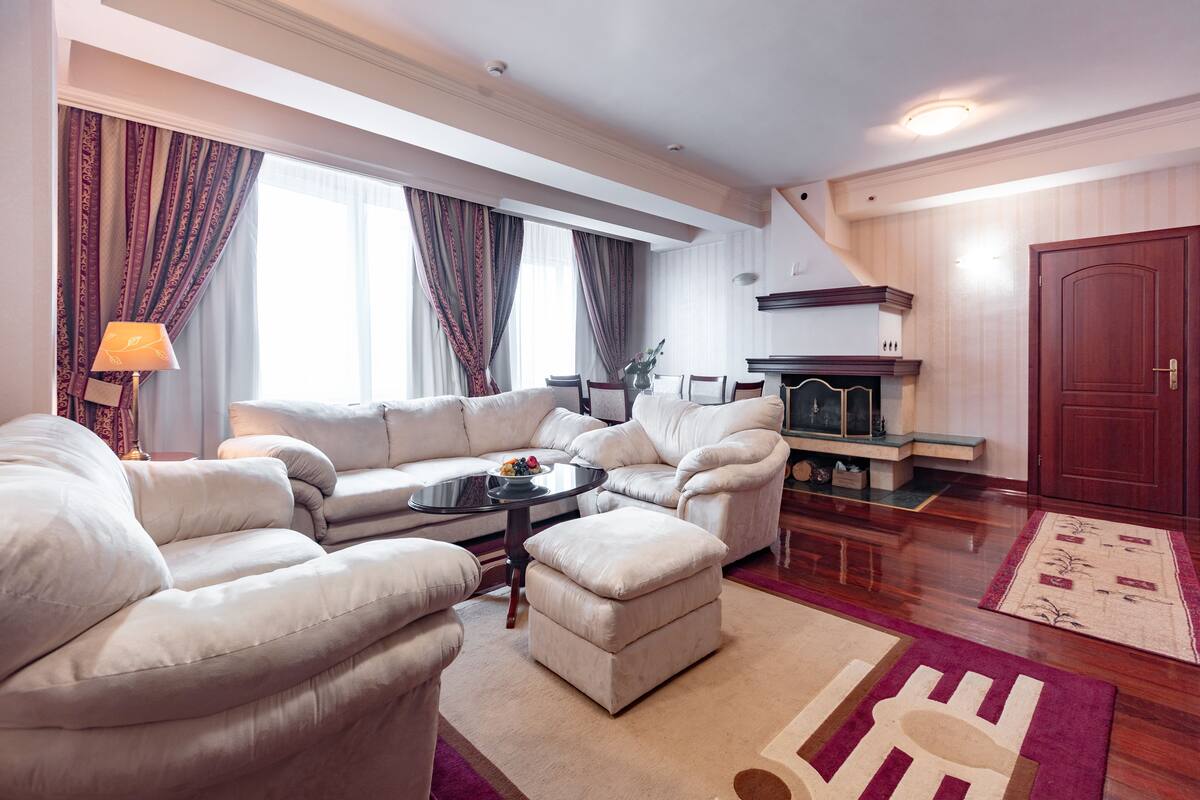 A spacious living room with a white sofa set, a coffee table, and a fireplace.