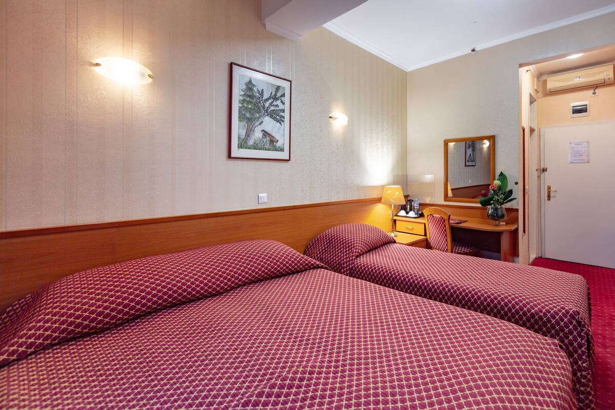 A hotel room with two beds, a desk, a chair, a mirror, and a door.