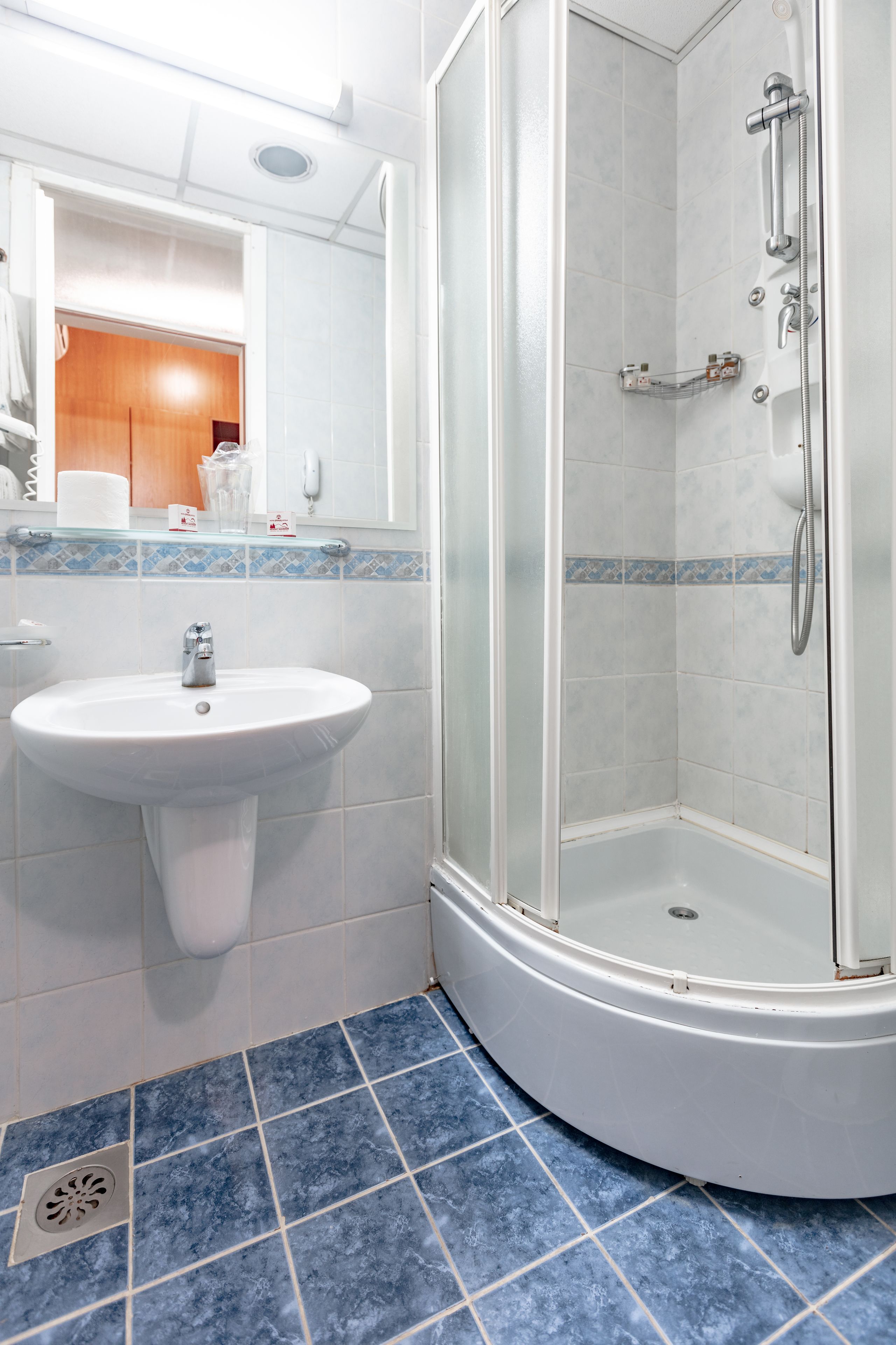 Un baño con lavamanos blanco, cabina de ducha con mampara de vidrio y suelo con azulejos azules.