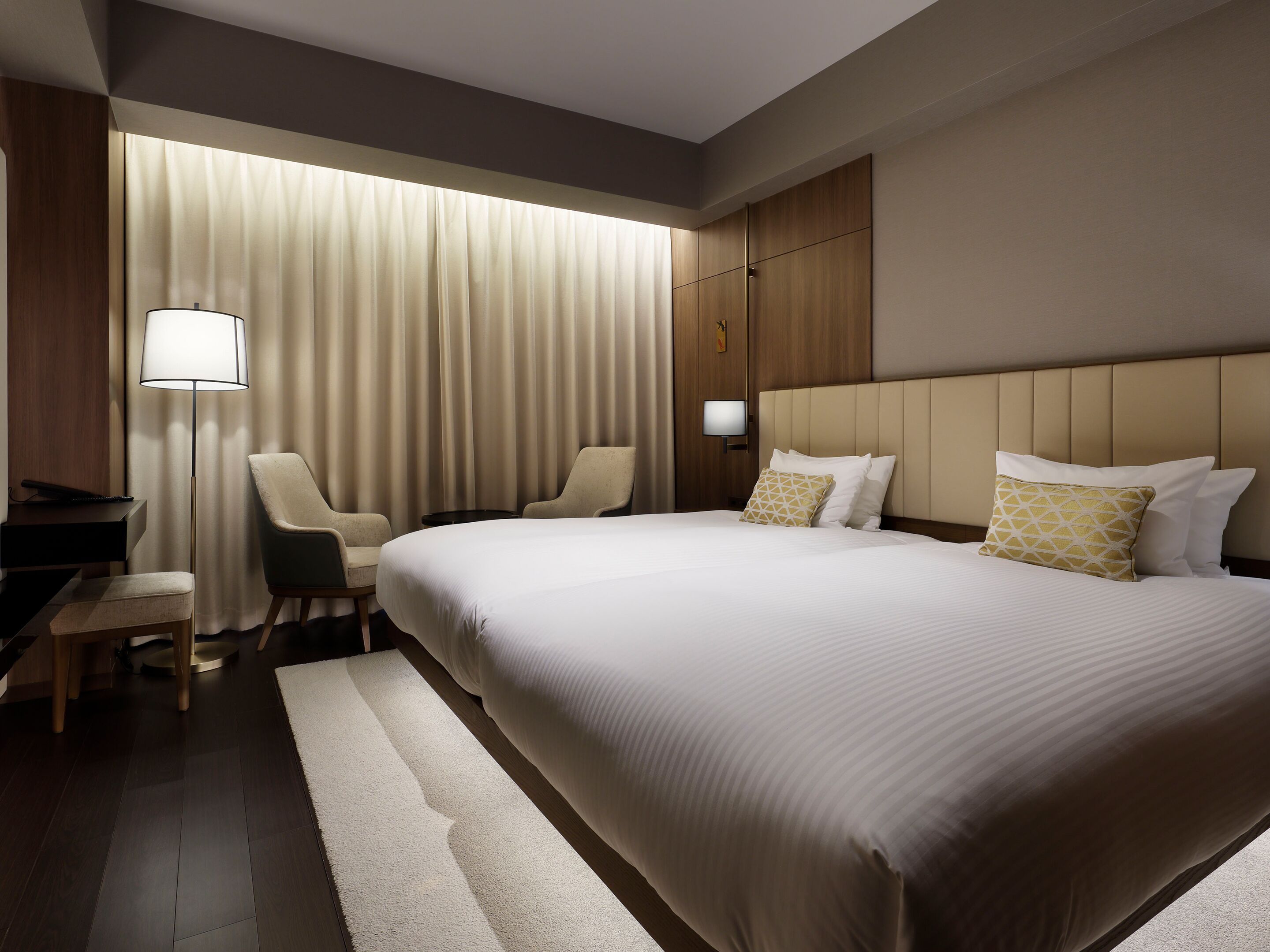 A hotel room with a large bed, a desk, a chair, a lamp, and a window with curtains.
