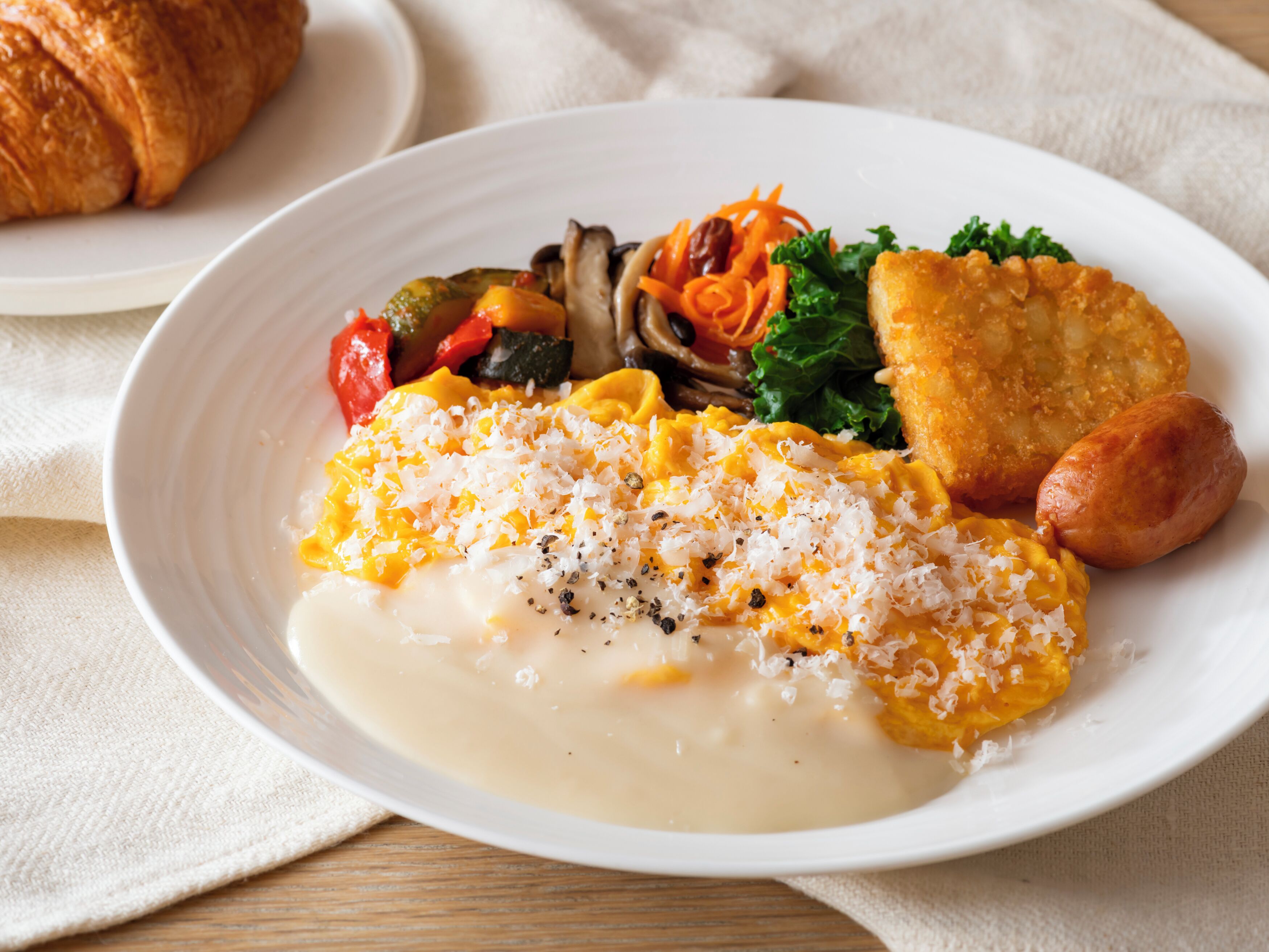 A plate of food with scrambled eggs, vegetables, and a croissant.
