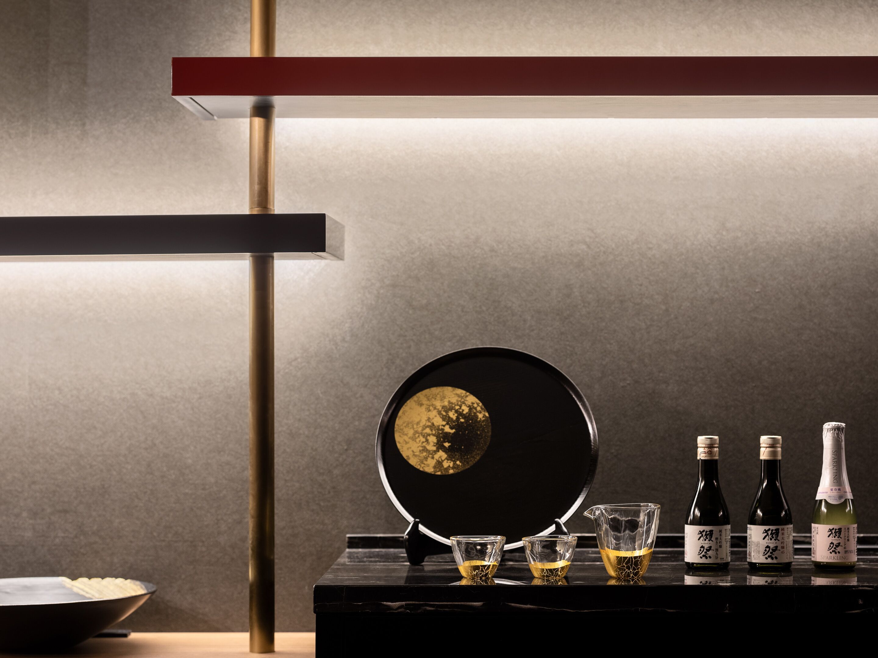 A modern kitchen with a black countertop, a frying pan, three glasses, and three bottles of sparkling wine.
