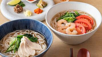Two bowls of noodle soup with various toppings, a small dish of condiments, and a pair of chopsticks on a wooden table.
