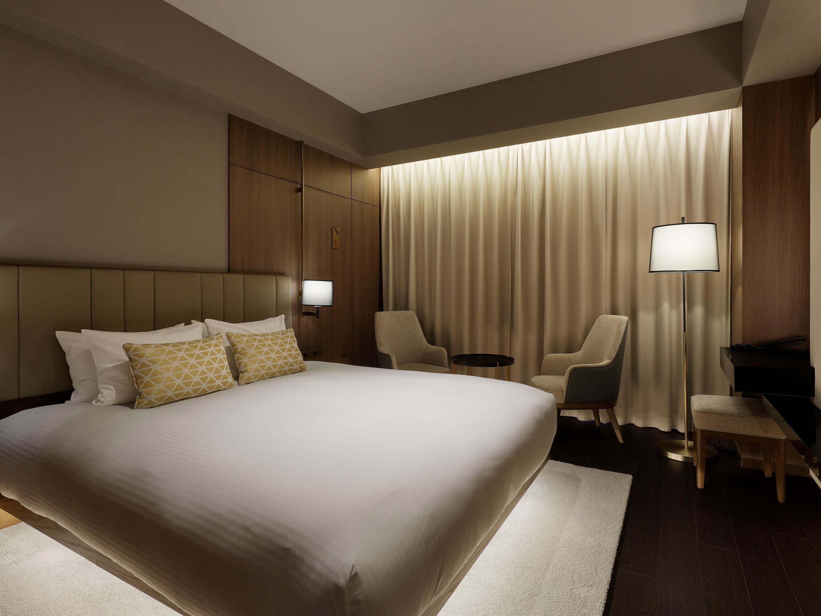 A hotel room with a large bed, two armchairs, a desk, and a lamp.