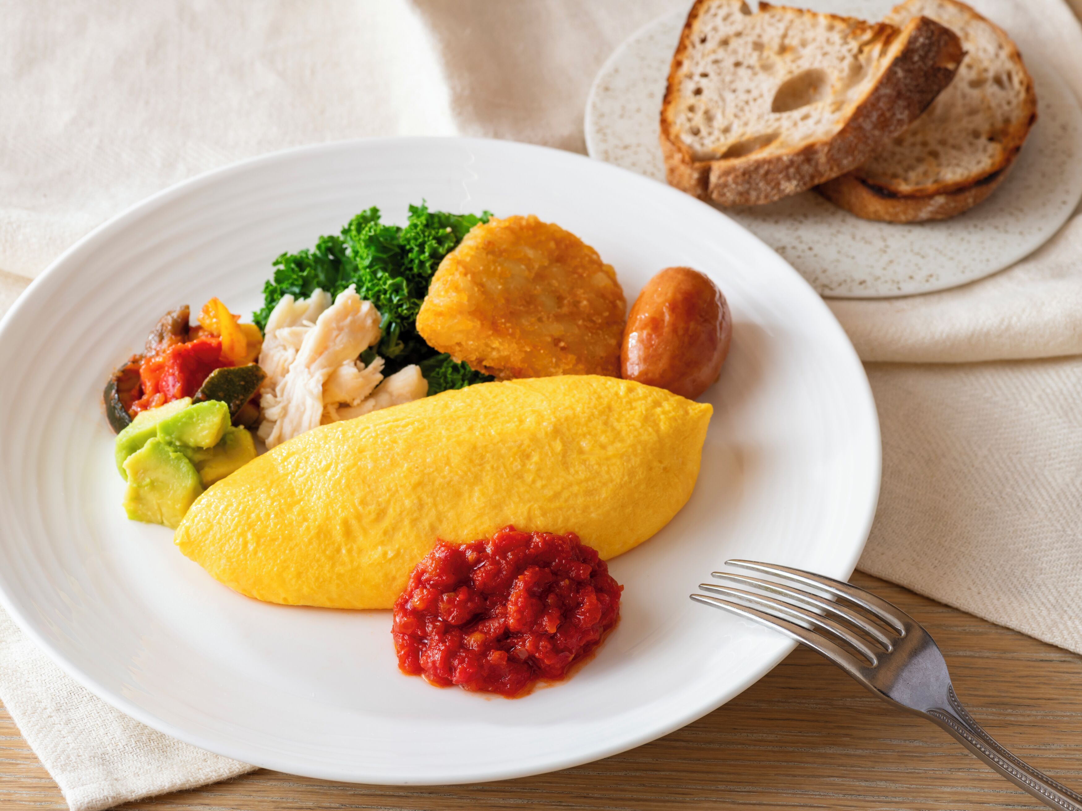 A plate with an omelette, vegetables, and a side of red sauce.
