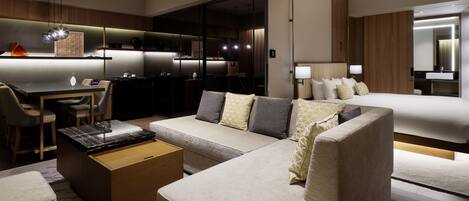 A modern hotel room with a sofa, a dining area, a kitchen, and a separate bedroom.