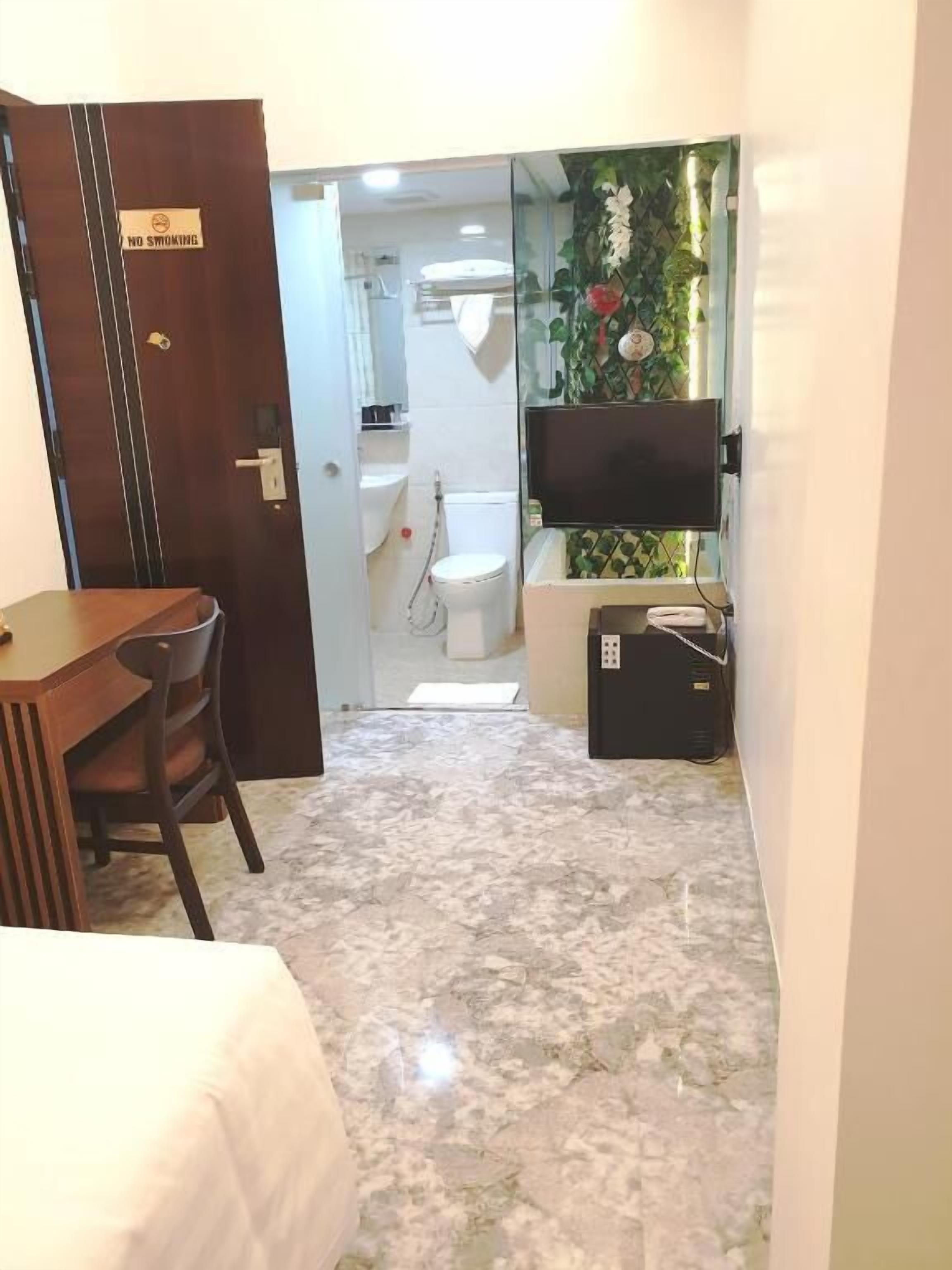 A hotel room with a wooden desk, a bed, a TV, and a bathroom with a toilet and sink.