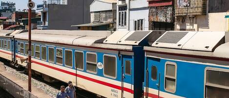 Un train circule sur des voies ferrées, avec un quai et un bâtiment en arrière-plan.