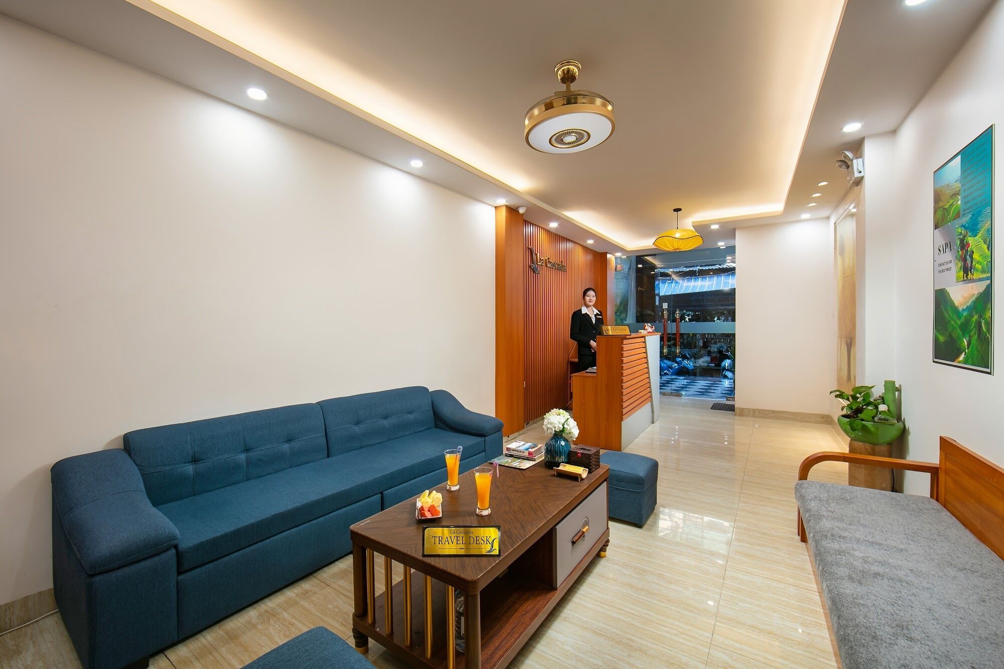 A hotel lobby with a reception desk, a blue sofa, a travel desk, and a wooden bench.
