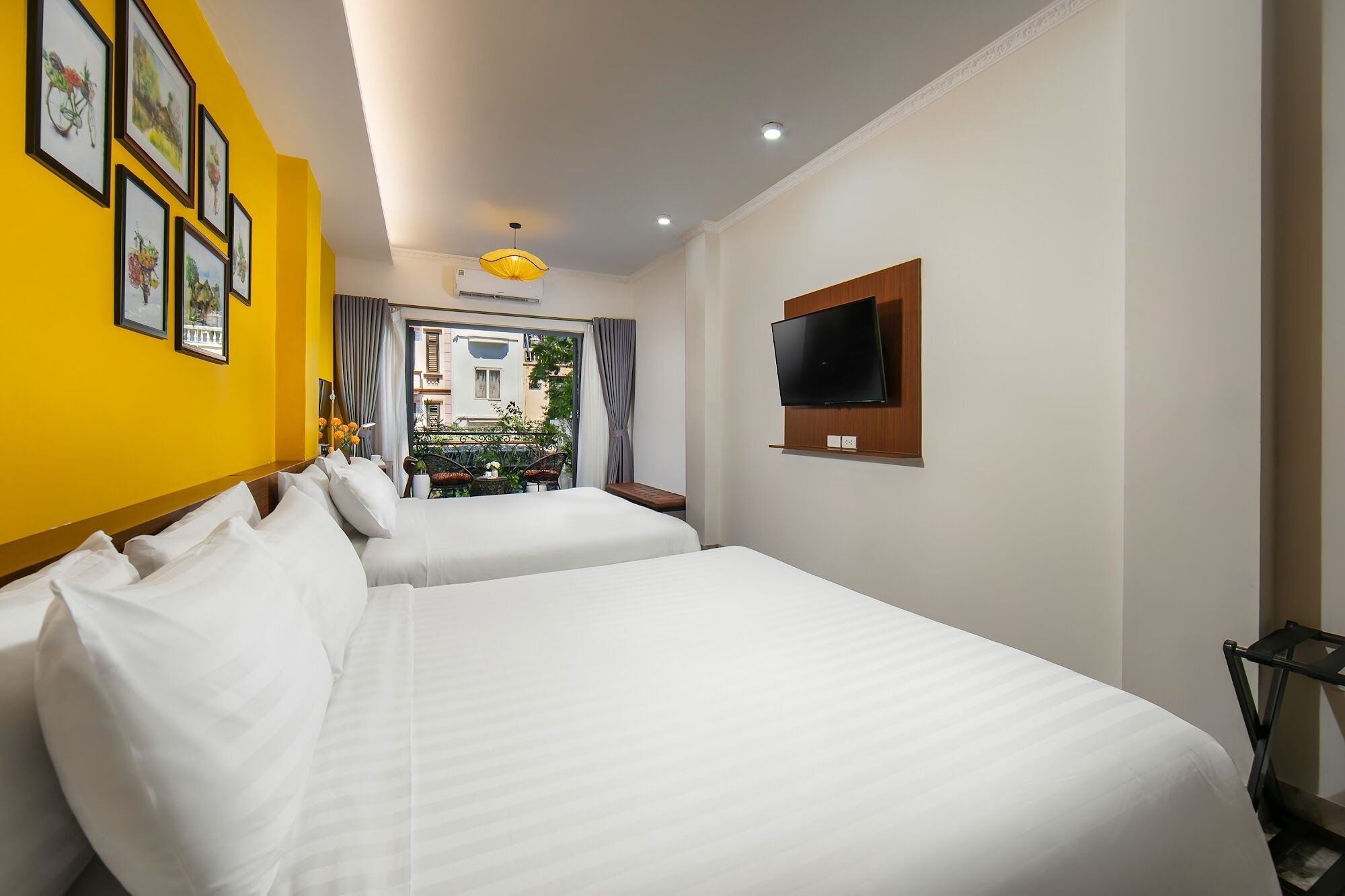 A hotel room with two beds, a TV, and a balcony with a view of the city.