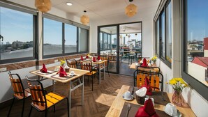 A modern dining area with large windows, wooden tables, and chairs. - Hanoi La Cascada House & Travel (Hanoi)