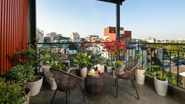 A balcony with wicker chairs, potted plants, and a view of the cityscape. - Hanoi La Cascada House & Travel (Hanoi)