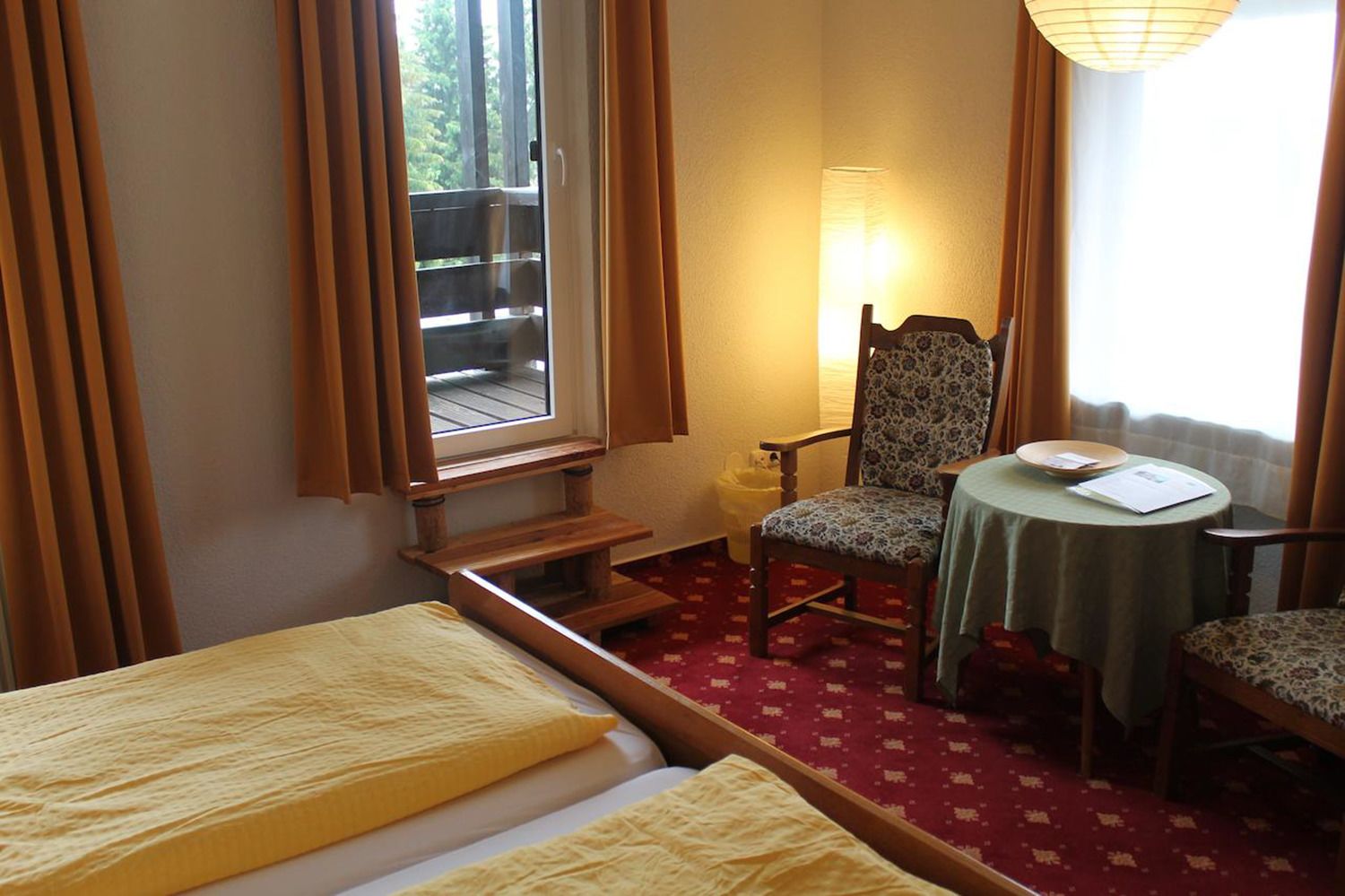 Una habitación de hotel con cama, una silla, una mesita y una ventana con cortinas.