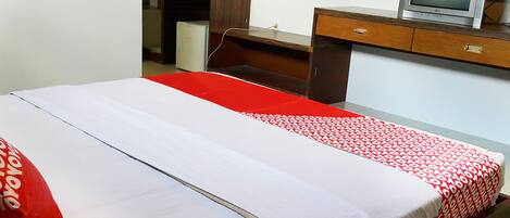 A bed with a red and white patterned bedspread, a red pillow, and a small bedside table with a television on top.