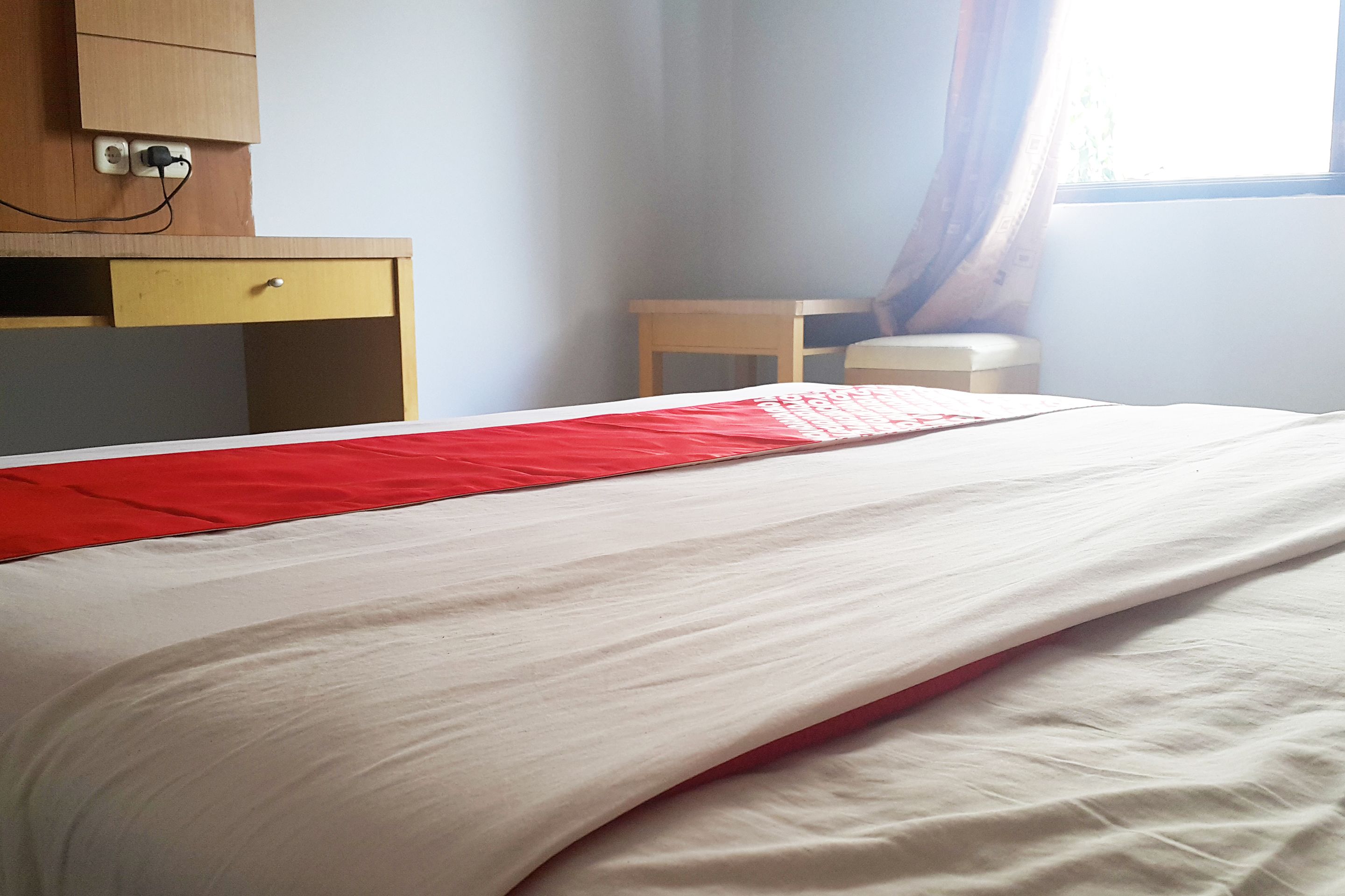 Una cama bien hecha con un corredor rojo, un escritorio de madera con un cajón y una silla.