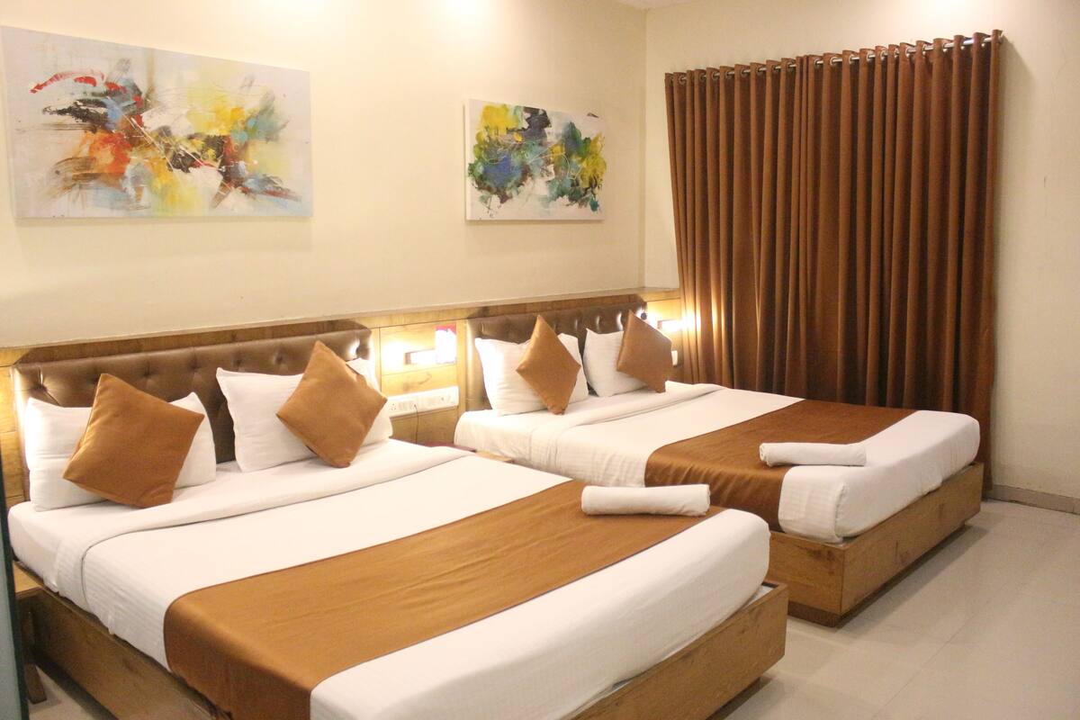 A hotel room with two beds, brown headboards, white linens, and two abstract paintings on the walls.