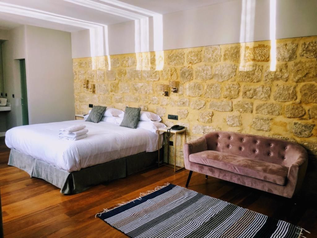 Un dormitorio con una cama grande, un sillón rosa, una pared de piedra y suelo de madera.